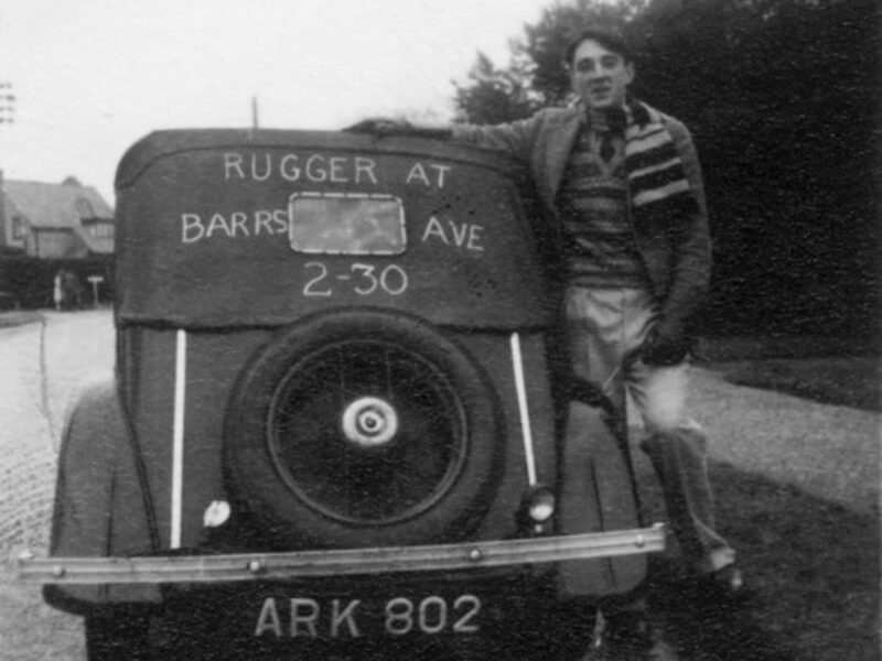 Historic photo of someone from New Milton Rugby Football Club next to a car that states Rugger at Barrs Ave 2:30